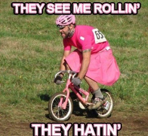 Cyclist attempting to ride comically small bicycle in grass wearing a pink dress