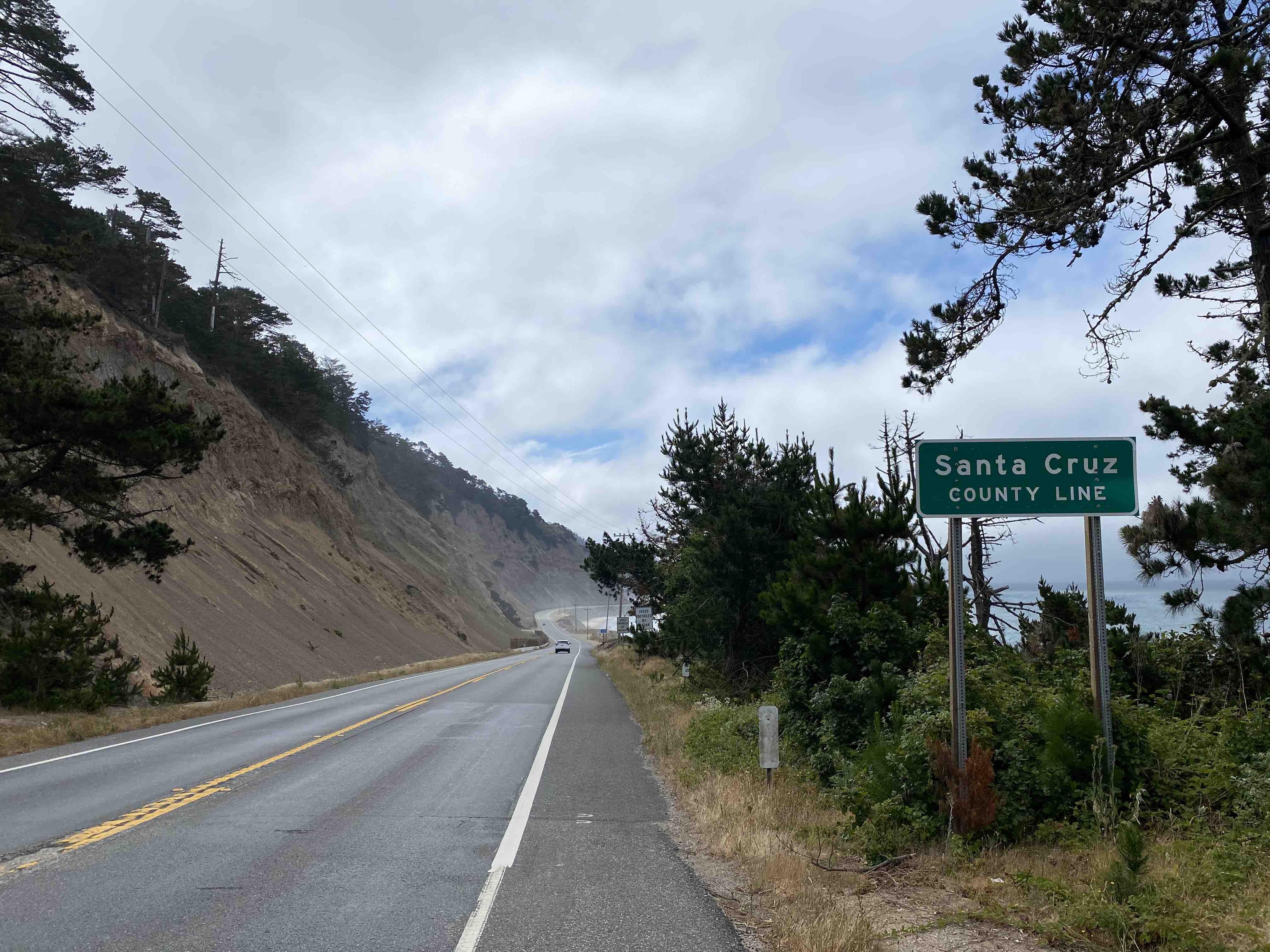 Santa Cruz county line road sign along road in front of mountains sloping into the ocean