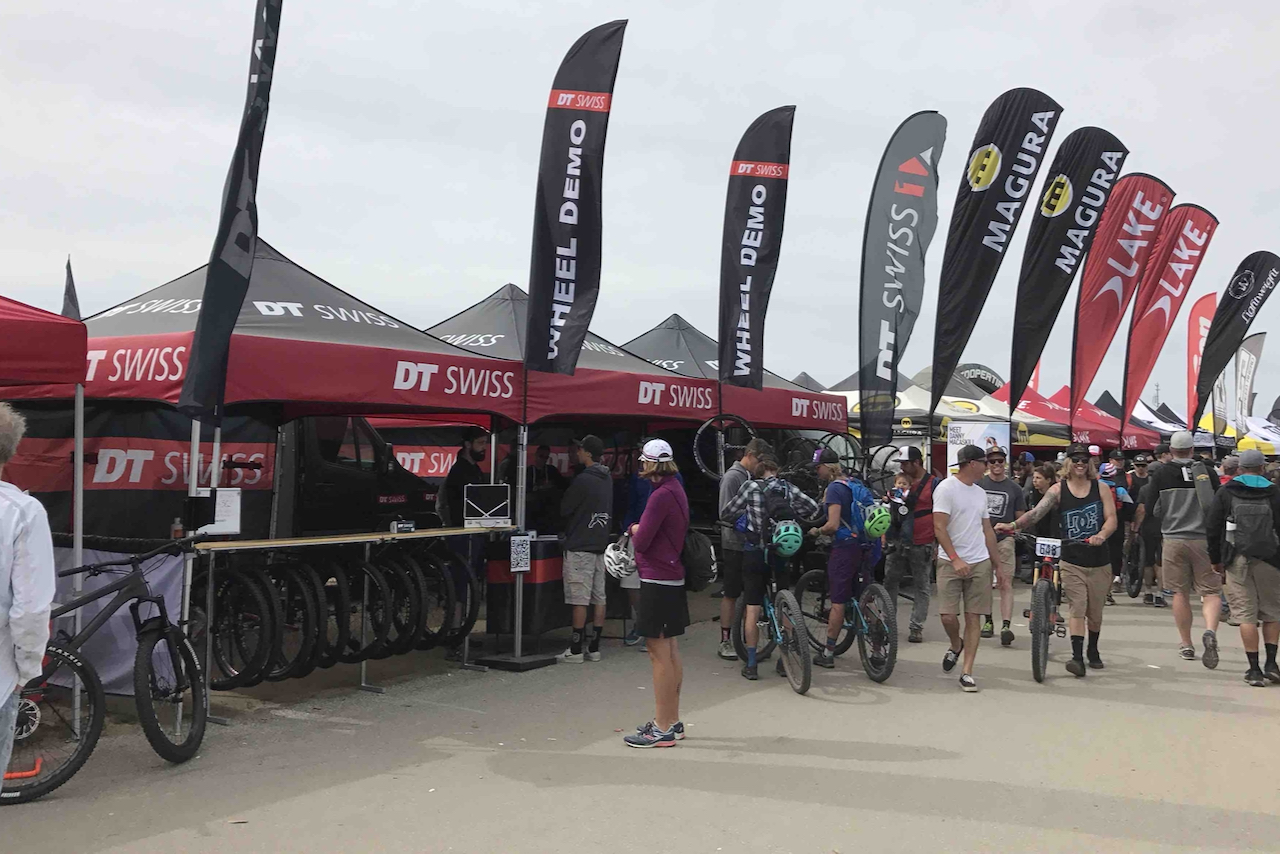 Understanding the marketing around bikes is important, and so is supporting your local bike shop. Image contains: banners for bike manufacturers, people walking, bicycles, tents showcasing new cycling related products, DT Swiss, Magura, Lake, and others.