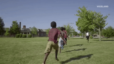 Children running along the grass towards some green trees