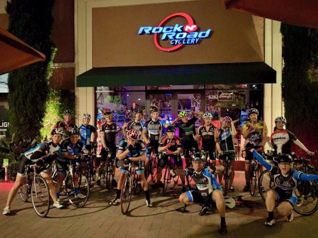A large group of bicycle riders posing outside of Rock n Road cyclery in Irvine, California
