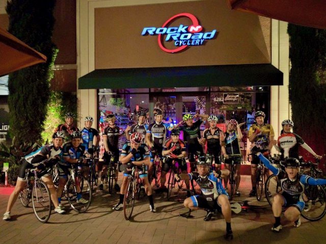 A large group of bicycle riders posing outside of Rock n Road cyclery in Irvine, California