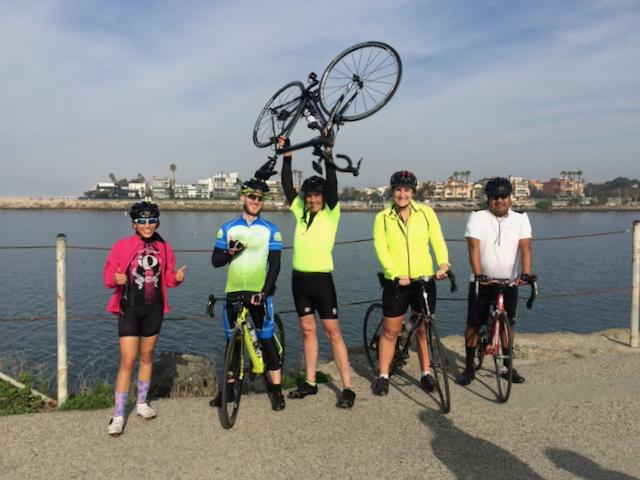 Several cyclists posing with their bikes overhead in Marina Del Rey