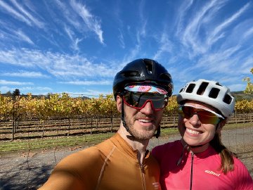 Two cyclists in helmets in front of a vineyard near Healdsburg, California