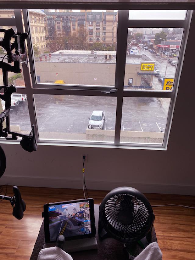 Indoor view of a Zwift trainer set up overlooking a rainy parking lot outside