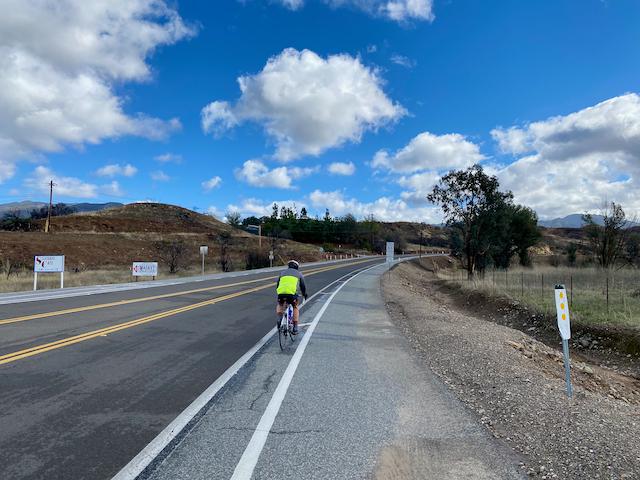 Cyclist riding along Santiago Canyon Road with soft clouds and blue skies
