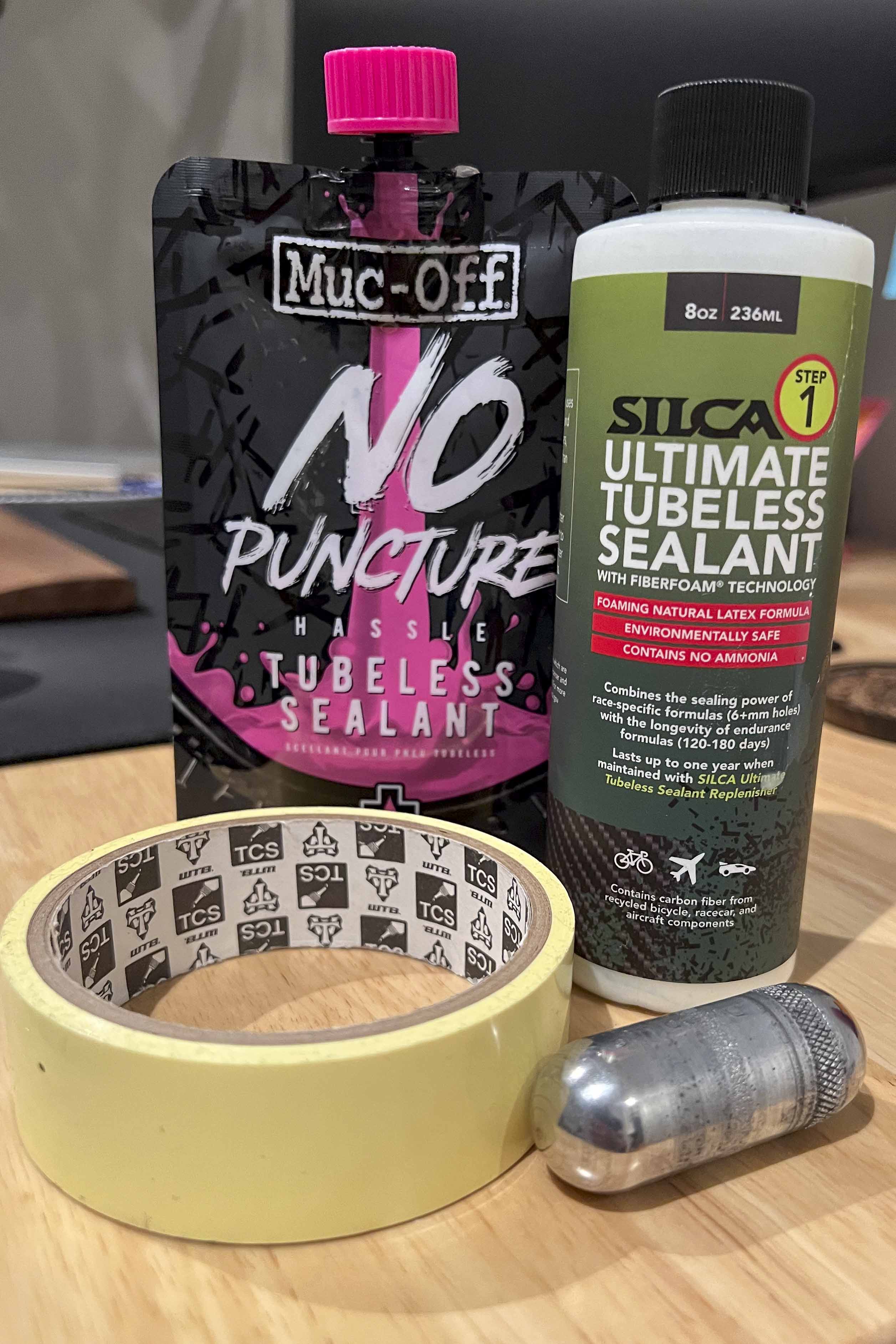 Featured bicycle tire tubeless products on a desk, including Silca, MucOff, rim tape, and a Dynaplug pill canister.