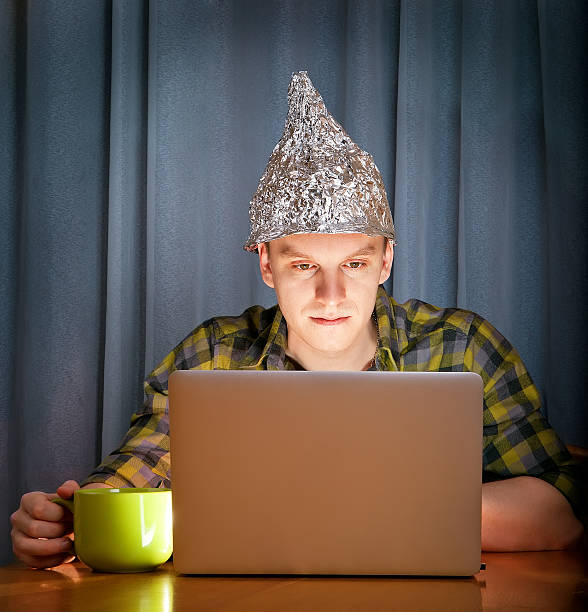 Stock image of a man at a computer wearing a tin foil hat