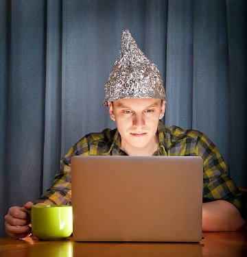 And down the rabbit hole we go! Stock image of a man at a computer wearing a tin foil hat
