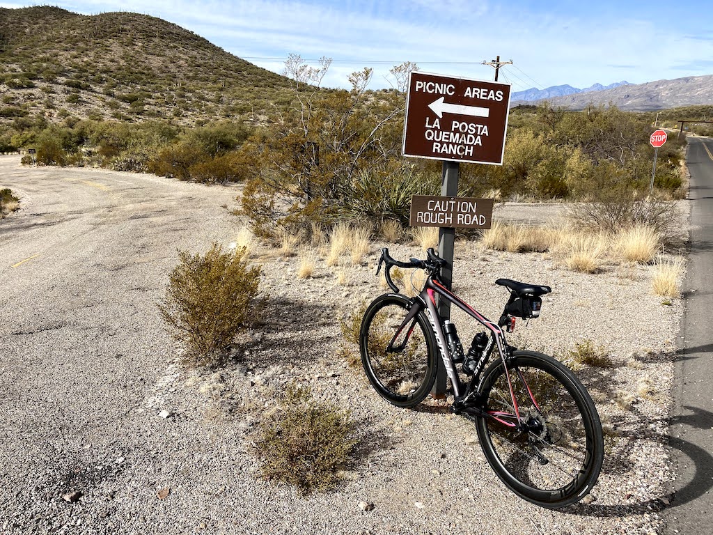 Bicycle leaning against a sign on Colossal Cave road saying rough road.
