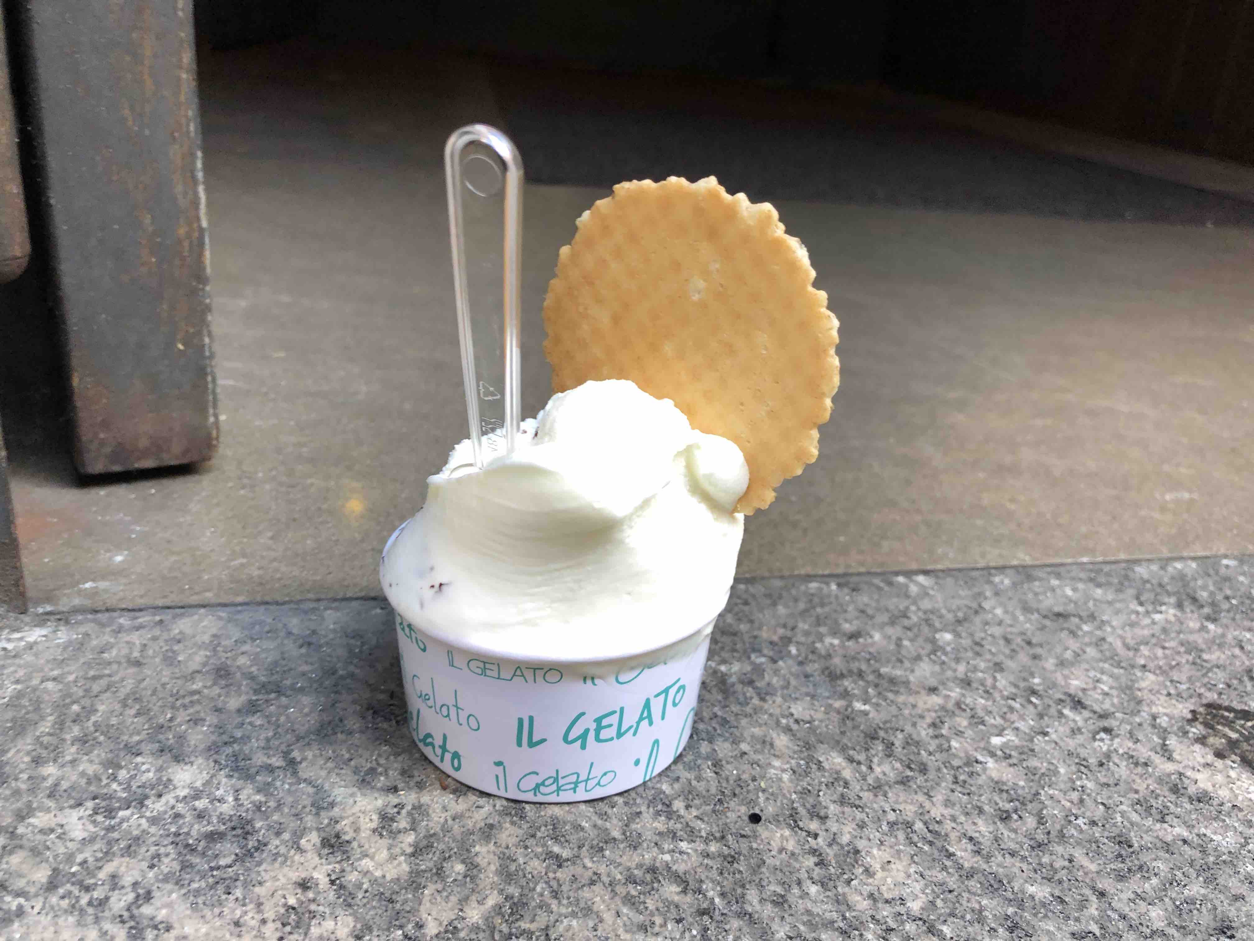 Gelato ice cream in cup with waffle cookie and spoon sitting on pavement