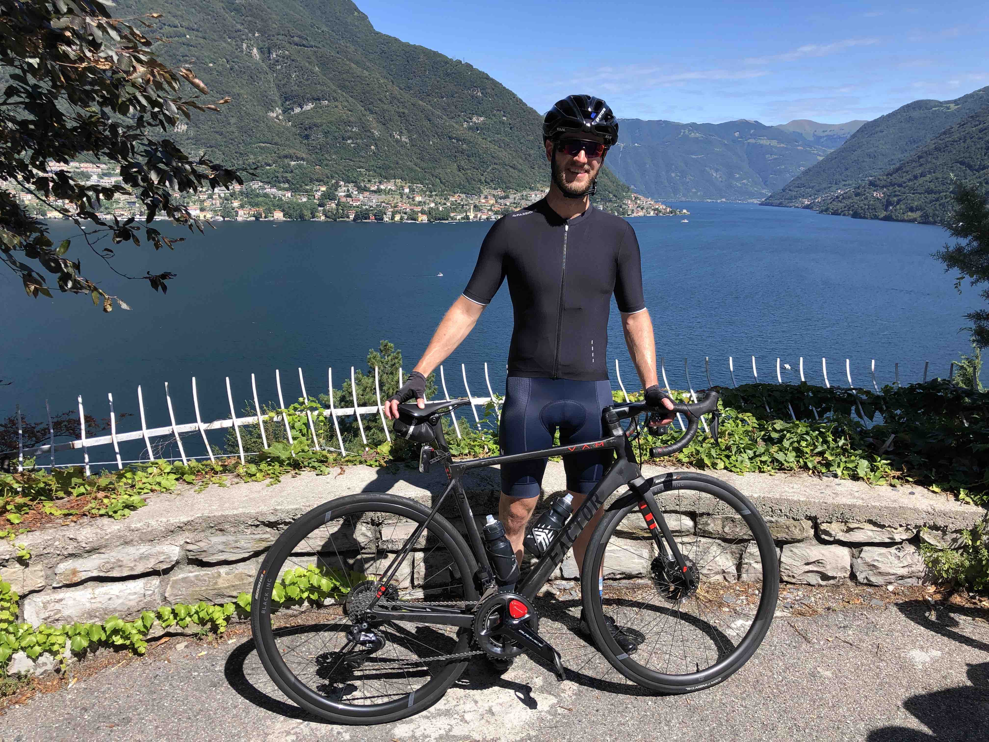 Cyclist posting with bike over a view out over Lake Como