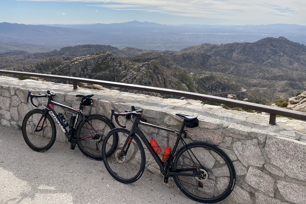 Mt. Lemmon, a high altitude challenge for any cycling enthusiast with rewarding views. Image contains: trees, views of Tucson Arizona, rocks, a railing, a winding road off in the distance.