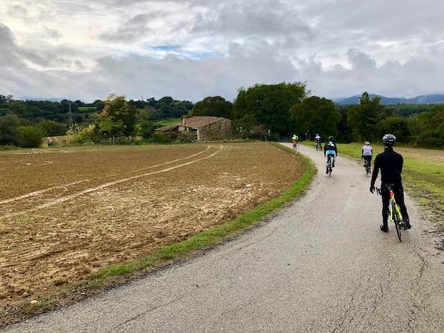 Cyclists riding into the distance with a view over a church in Can Sisi Masia near Girona