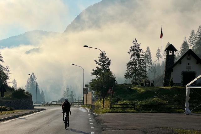 Cyclist descending from the Passo Fedaia through fog and morning light