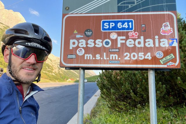 Cyclist with helmet at the Passo Fedaia sign near Alleghe, Italy