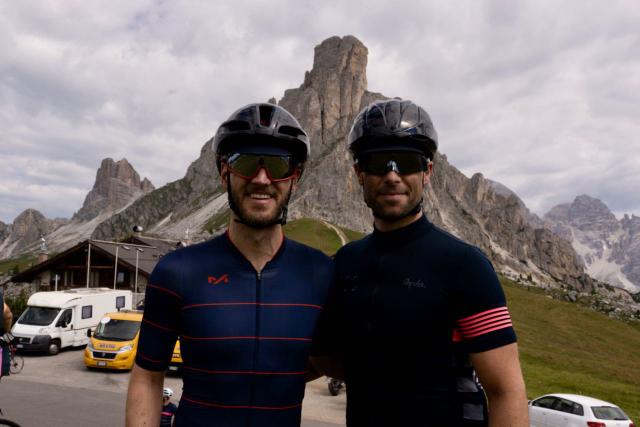 Two cyclists posing by the road sign at the top of the Passo Giau