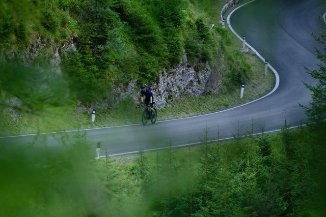 Cyclist climbing the Passo Giau in the Italian Dolomites, viewed through the trees