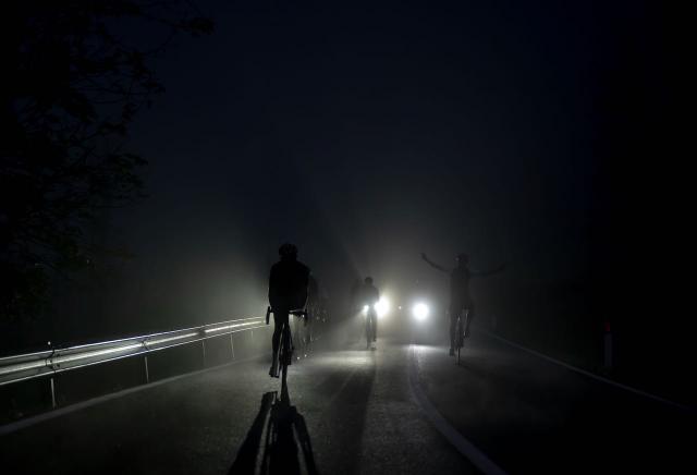 Cyclists riding by headlights before dawn in Alleghe, Italy