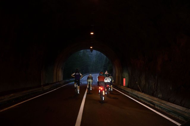 Cyclists riding through a tunnel on the way up to the Passo Fedaia in the morning light