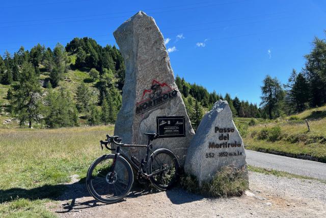 Factor O2 VAM bicycle leaning against the Mortirolo marker at the top of the climb