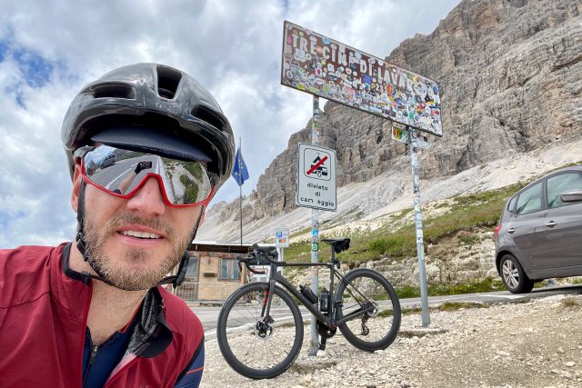 Cyclist posing with sticker filled sign at the top of the Tre Cime di Lavaredo