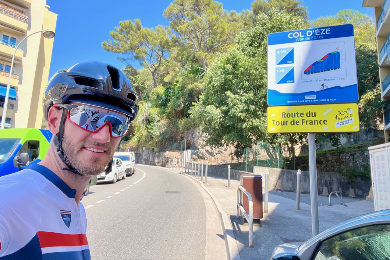 Cyclist standing in front of climb profile sign at the base of Col d'Éze in Nice, France