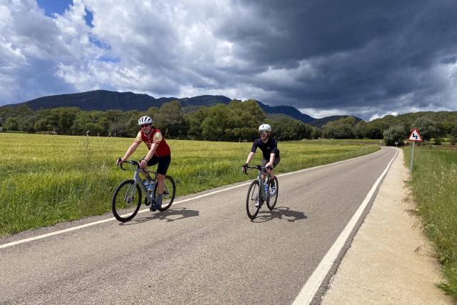 Cyclists riding near Canet d'Adri in Girona, Spain, with rain clouds in the background.