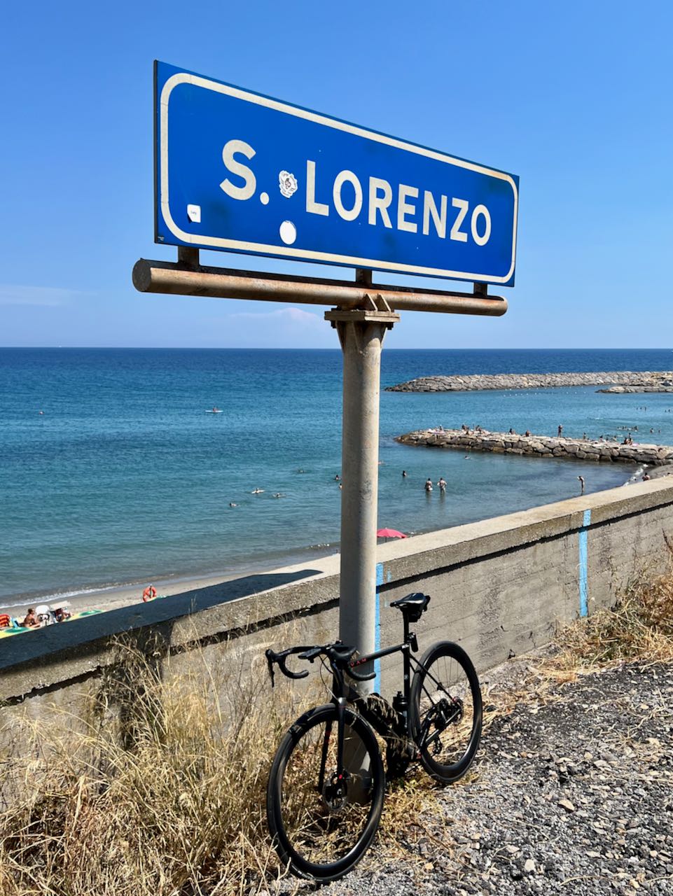 Bicycle leaning against San Lorenzo city sign with ocean and swimmers in the background