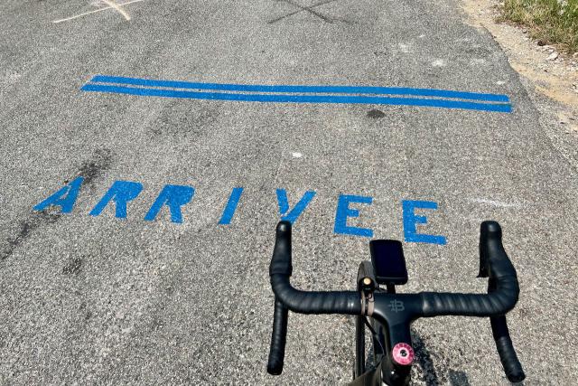 Arrivée written in pavement at the top of the Col de la Madone with bicycle handlebars in view