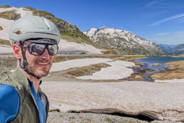 Cyclist selfie at the top of the Sustenpass with snow in the background in summer