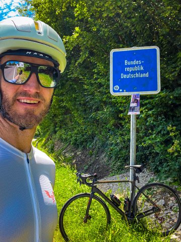 Cyclist selfie with a blue Deutschland country sign on the border with Germany