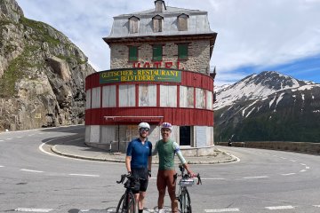 Two cyclists posing in front of the Hotel Belvedere on the Furkapass near Gletsch, Switzerland