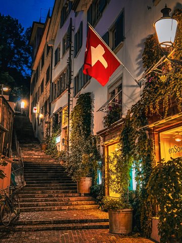 Auf wiedersehen, Switzerland! Swiss flag flying over night-lit shops in Zürich, Switzerland